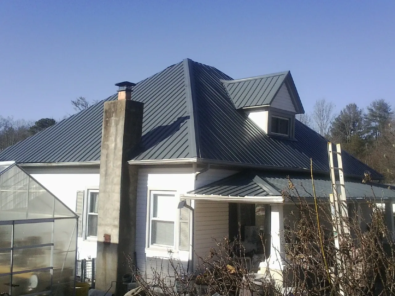 Dark blue standing seam metal roof on a white farmhouse with dormer — Slate & Tile Roof Repair by Roofing Brothers in Nolensville