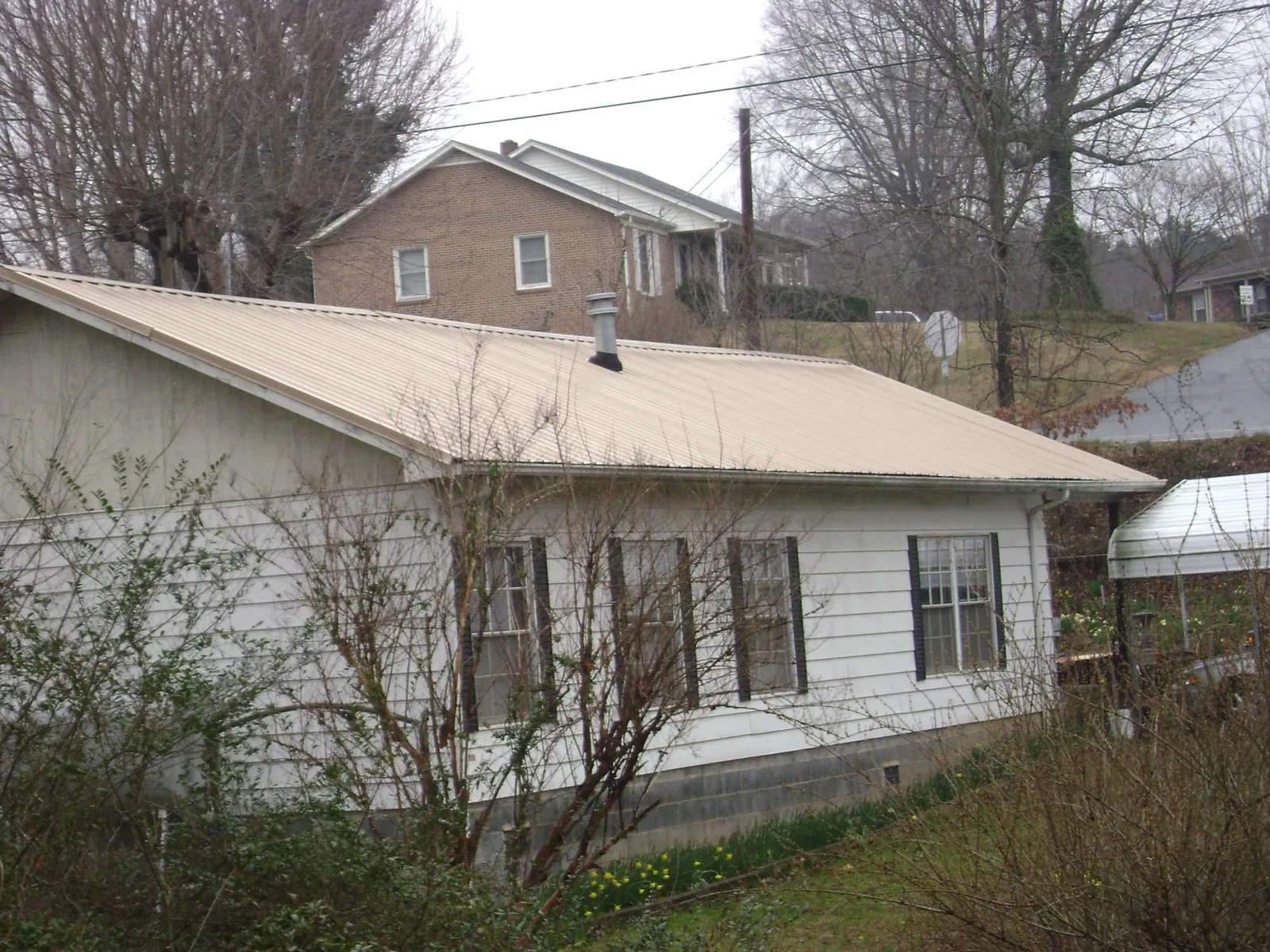 Tan metal roof on a white sided house set into a hillside — Commercial Roofing by Roofing Brothers in Nolensville